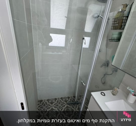 מקלחת עם דלת זכוכית, ראש מקלחת ומדף עם מוצרים